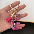 Detalle del llavero letra E de resina rosa con anillo dorado, borla y bola de lentejuelas - Cierre De Borla De Bola Pequeña / Letra E