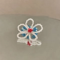 Détail d'une bague en perles faite main en forme de fleur avec reflet sur miroir poli - Bague Fleur / Bleu-Blanc