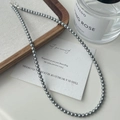 Elegante grijze faux parelketting getoond naast een parfumflesje en een houten dienblad - 4mm Grijze Parel