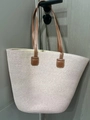 Off-white woven straw tote bag with slim brown straps hanging on a grey door handle - Pure Pink