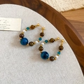 Detailaufnahme von Tigerauge-Ohrringen mit Perlen auf Leinen- und Holzhintergrund - Gold-Blau