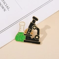 Detalle de un pin esmaltado científico con un microscopio y un frasco de laboratorio - Microscopio y Matraz / Verde/Negro/Dorado