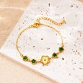 Detailed shot of gold plated bracelet with green star stones and flower charms on stone - Sunflower & Green Star Style