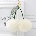 Close-up of white cherry-shaped faux fur keychain with green leaves and gold clasp - Off White