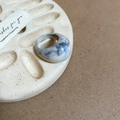 Detail eines marmorierten Harz-Ovals-Rings auf elegantem Keramiktablett mit Papier - Weißes Marmormuster