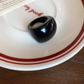 Dettaglio di un anello in resina nera lucida su un piatto di ceramica stile vintage - Nero