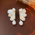 Detailed close-up of gold flower butterfly earrings with white pearls on leather texture - Long White Petal Drop Style