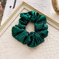 Close-up of dark green metallic scrunchie with pleated texture on magazine background - Glossy Green