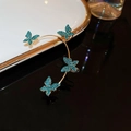 Dettaglio ravvicinato di un ear cuff dorato con quattro farfalle di cristallo blu lucenti - Gancio per Orecchio a Farfalla con Strass Blu (36#) / Blu
