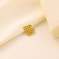 Dettaglio del ciondolo dorato lettera B su sfondo elegante in seta color beige - Lettera traforata B