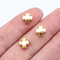 Tre piccole perline a croce in metallo dorato per gioielli esposte su un polpastrello - Oro Lucido