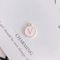 Close-up of a pink enamel round charm featuring a golden letter V for DIY jewelry making - Letter V