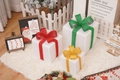 Three white Christmas gift boxes with red green and gold glitter ribbons on plush rug - White Long Plush Christmas Gift Box