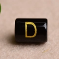 Macro detail of a black cylindrical bead featuring a gold-stamped letter D for DIY jewelry - Letter D