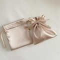 Close-up of champagne satin drawstring gift bags with silk ribbon bow on white texture - 12x14cm / Champagne Gold