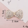 Macro shot showing dimensions 2.6cm x 1.5cm of a gold bow-knot with white rhinestones - D116 Small Bowknot