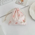 Detailed view of pink plaid cotton drawstring pouch with red bow print on a white desk - Pink Gingham Bow