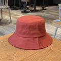 Detailed view of rust red cotton bucket hat with fine stitching on a wooden surface - One Size / Brick Red
