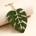 Macro shot of green monstera leaf keychain with gold metal frame on a display stand - Emerald Geometric Stripe Monstera Leaf / Green Plaid
