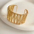 Detail eines vergoldeten Wickelarmbands mit Metalldraht-Textur auf weißer Keramik - Gold