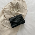 Chic black quilted crossbody bag with luxury pearl chain strap on beige blazer - Black