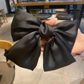 Elegant black satin oversized bow hair clip held by hand against a blurred café backdrop - Large / Black Spring Clip