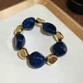 Macro view of irregular blue acrylic beads with gold metal accents on a white tray - Bracelet / Blue