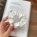 Close-up of a white cotton scrunchie on a magazine page showing soft fabric texture - White