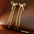 Dettaglio degli orecchini a fiocco in oro 18k con nappe di cristallo su pelle marrone - Perno in Argento Oro (Placcatura in Oro Vero) / Oro