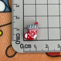 Macro shot of a 2cm mini red resin Christmas stocking charm next to a measuring ruler - Socks