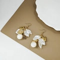 Primer plano de los pendientes de pétalos blancos con mariposa dorada y perla elegante - Mariposa