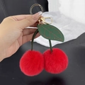 Détail du porte-clés cerise en fausse fourrure rouge avec feuille en cuir en main - Rouge
