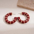Macro view of vintage red enamel C-shape stud earrings with gold striped texture - Red