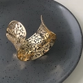 Detailaufnahme des goldenen breiten Armreifs mit asymmetrischen organischen Hohlmustern - Goldenes hohles geometrisches Armband