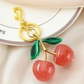 Close-up of glittery red resin cherry keychain with golden lobster clasp and green leaves - Gold Green Double Leaf Pink Cherry