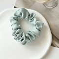 Close-up of a light blue satin scrunchie with silky luster on a minimalist white plate - Light Green
