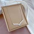 Macro view of silver V-shaped pendant with inset crystals on a golden textured box - Silver