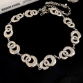 Dettaglio macro di anelli metallici argentati intrecciati con strass bianchi e chiusura a moschettone - Argento