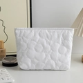 Detailed close-up of a white quilted floral pattern on a portable travel makeup pouch - White