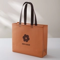 Orange non-woven boutique shopping bag with dark brown handles and floral logo - 28*32*10cm / Caramel color