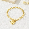 Bracciale dorato minimalista con ciondolo a cuore e chiusura OT su superficie bianca - Bracciale con chiusura a T / Oro