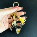 Macro detail of resin letter N keychain with white dried flowers and gold bee charm - Letter N