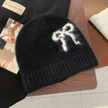Close-up of black mohair knit beanie featuring a white bow pattern on a wooden surface - Bow Pattern / Black