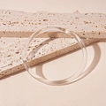 Vista macro de un brazalete de acrílico transparente sobre fondo de piedra beige - Brazalete-Transparente