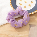 Detail view of purple chiffon hair scrunchie with gold heart pattern on wooden surface - Purple