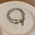 Dettaglio macro di perle in agata con campanellino d'argento e ciondolo portafortuna su piatto - Blu Stile Pace (64#)