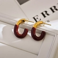 Close-up of gold and burgundy C-shaped stud earrings on a white leather texture display - Brown