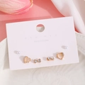 Detalle del set de pendientes de corazón rosa, lazo de strass y perla en cartón blanco - Juego de Lazo de Corazón de Piedra de Ojo de Gato Dorado (1940) / Dorado