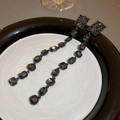 Close-up of elegant long drop earrings with dark grey gemstones on a ceramic plate - Silver Pin Black Style (HE8740)