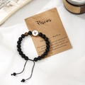 Close-up of black beaded Pisces zodiac bracelet with adjustable cord on white fabric - Pisces